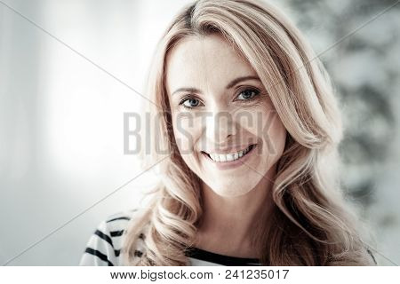 Good Mood. Pleasant Cute Blonde Woman Being In The Bright Room Standing And Smiling.