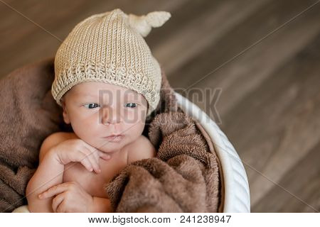 A Little Child In A Beige Cap Lies In The Basket