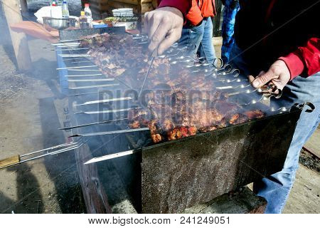 Meat On Skewers Fried On The Grill In The Open Air, Visible Hands Of The Cook