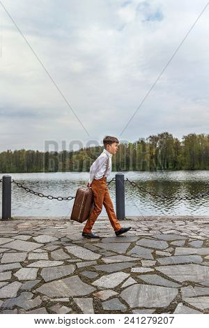 Rustic Guy In Old-fashioned Clothes Paces On The Pier With A Huge Retro Old Suitcase