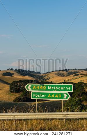 Signs On The South Gippsland Highway Pointing Towards Foster And Melbourne, Among The Rolling Hills 
