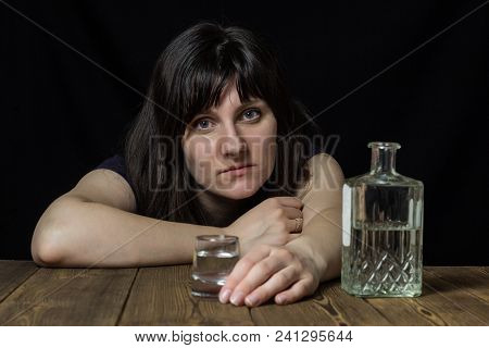 Girl At The Table With Alcohol In Hands, Black Background, Looks At The Camera
