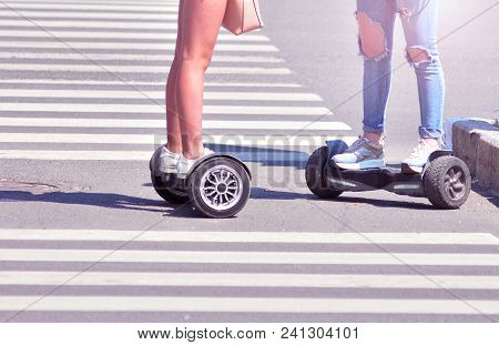 Two Girls On Gyro Boards Stops On A Pedestrian Crosswalk