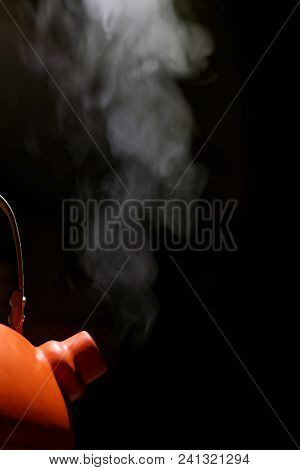 Orange Kettle With Boiling Water And Steam Escaping From The Spout Against Black Background.