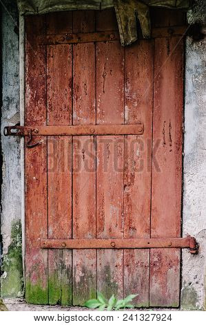 Old Wooden Door Is Not Closed On The Lock. Peeling Paint. House. Barn. Doors Red. Covered With Moss.