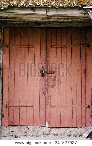 Old Wooden Door Closed On The Lock. Peeling Paint. House. Barn. Doors Red. The Door To The Hinges.