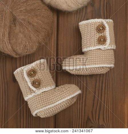 Baby Booties Knitted By Hand On A Wooden Background And Skeins Of Wool