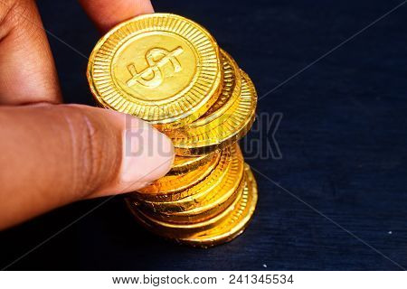 Black Skin Finger Hold Gold Coin With Dollar Currency Write On It. Gold Coin On Black Background