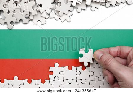 Bulgaria Flag  Is Depicted On A Table On Which The Human Hand Folds A Puzzle Of White Color.