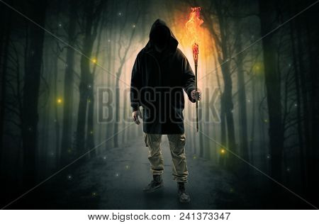 Mysterious man coming from a path in the forest with burning flambeau concept