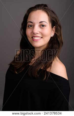Studio Shot Of Young Happy Beautiful Woman Smiling While Wearing Black Off-shoulder Top Against Gray