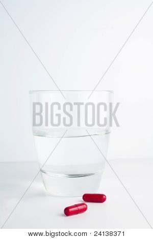 Rote Tabletten neben einem Glas Wasser