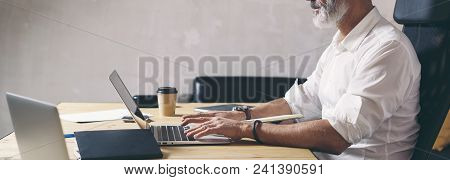 Attractive And Confidental Adult Businessman Using Mobile Laptop Computer While Working At The Woode