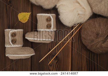 Baby Booties Knitted By Hand On A Wooden Background And Skeins Of Wool