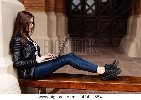 Smiling Student Girl Sitting On Bench In Park, Working With Laptop And Taking Notes, Preparing For E