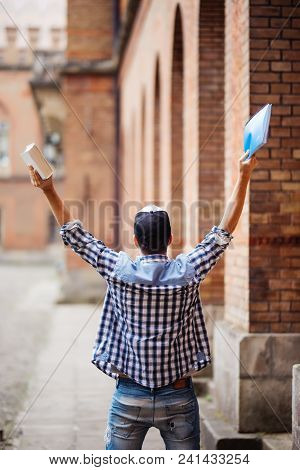 Young Man Student With Raised Hands Of Sucess In Front Of Uni Campus. Young Man Happu Victory Of Pas