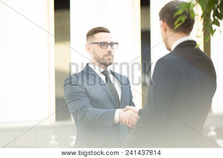 Two young business partners shaking hands and greeting one another after striking successful deal