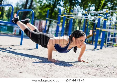 Young Sportive Woman Trainer In A Bright Blue Sport Bra And Black Leggings Doing Push Ups On The Spo