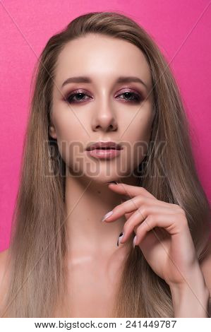 Beautiful Young Girl With Bright Pink Make-up And Combed Hair On A Pink Background Looks Into The Fr
