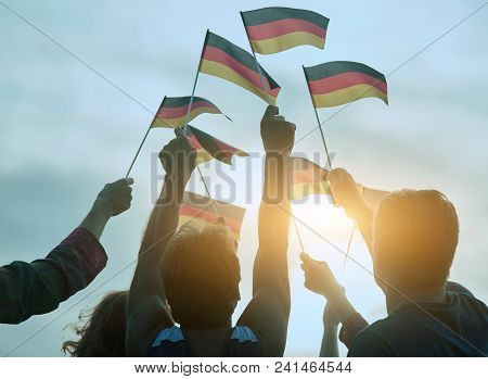 German Flags Gathering. Raising Small Deutsch Flags To The Blue Sky, Back View.