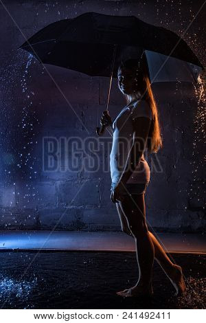 Girl In The White Shirt With Black Umbrella, Water Drops Around And Dark Walls Background Illuminate