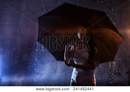 Girl In The White Shirt With Black Umbrella, Water Drops Around And Dark Walls Background Illuminate