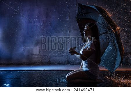 Girl In The White Shirt With Black Umbrella, Water Drops Around And Dark Walls Background Illuminate
