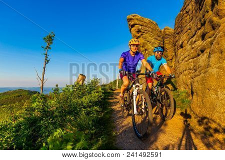 Mountain biking women and man riding on bikes at sunset mountains forest landscape. Couple cycling MTB enduro flow trail track. Outdoor sport activity.