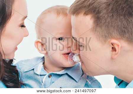 Baby On The Hands Of Parents On A White Background. Dad Takes A Mouth A Pacifier From A Baby