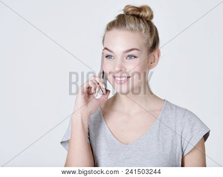 Close up portrait of a happy woman talking on the mobile phone on gray bacjground