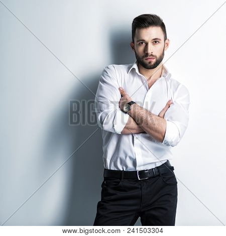 Handsome man in white shirt and black trousers - posing  at studio. Attractive guy with fashion hairstyle.  Confident man with short beard. Adult stylish boy with brown hair.
