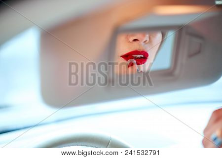 Beautiful Girl Driving A Car Paints Lips With Red Lipstick.