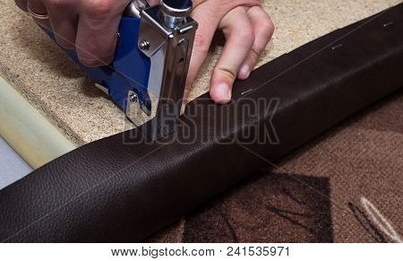 Craftsman Fastening Brown Leather To The Paricle Board Using Staples And Blue Stapler