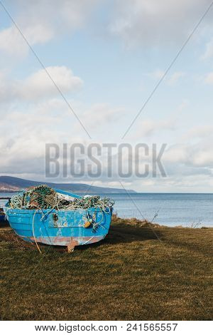 An Unidentified Blue Wooden Fishing Boat Full Of Fishing Nets On The Grass By The Shore In Brora, Sc
