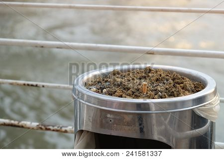 Cigarette Stub Buried In The Pile Of Wet Sand At Top Of Metal Trash Bin