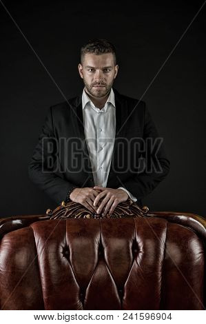 Confidence And Charisma. Man Stand At Leather Armchair On Dark Background. Bearded Man In Formal Sui