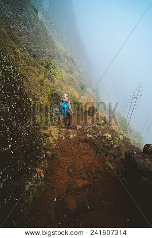 Hiker Women With Backpack Walking Down The Trekking Path. The Steep Arid Slope Of The Rock. The Fog 