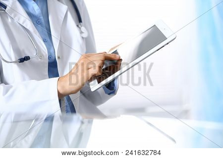 Woman Doctor Using Tablet Computer While Sitting. Reflecting Glass Table Is A Working Place Of Physi