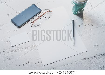 Mockup Of Blank Sheet Paper, Smartphone, Eye Glasses And Two Empty Business Cards On White Wooden De