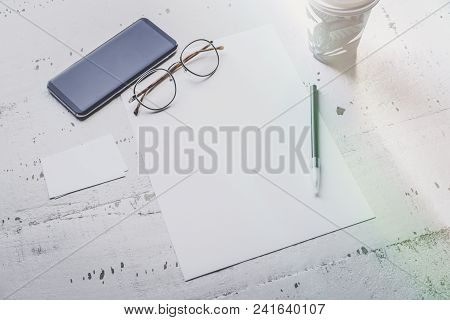 Mock-up Of Blank Sheet Paper, Smartphone, Eye Glasses And Two Empty Business Cards On White Wooden D