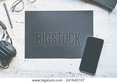 Mockup Of Blank Black Paper Sheet, Mobile Phone, Eye Glasses, Headphones On Natural White Authentic 