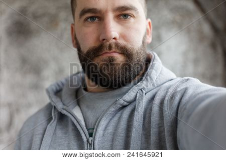 Bearded Man On A Gray Background Makes A Selfi