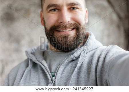 Bearded Man On A Gray Background Makes A Selfi