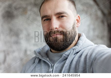 Bearded Man On A Gray Background Makes A Selfi