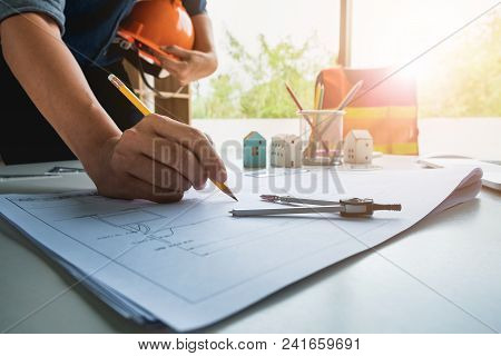 Hands Of Architect Or Engineer With Helmet Using Pencil Working With Blueprint On Desk In Office . E