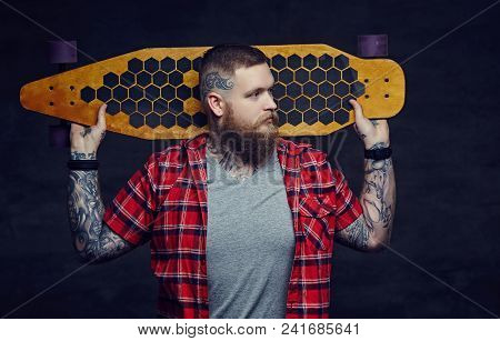 Bearded Man With Tattooes On His Arms Holding Longboard.