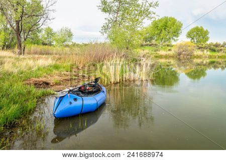a blue pacraft (one-person light raft used for expedition or adventure racing) with a kayak paddle on a lake shore in spring scenery