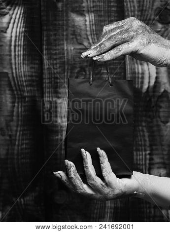 Female Hands Smeared In Golden Paint Or Glister Holding Black Selective Focus Package Or Bag On Brow