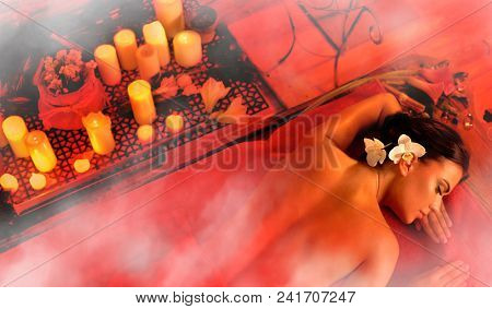 Massage of woman in spa salon. Top view of girl on candles aglow background in steam room. Luxary interior in oriental therapy salon. Photo effect with red toning.