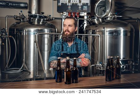 Portrait Of Tattooed, Bearded Hipster Male Manufacturer Presenting Beer In The Microbrewery.